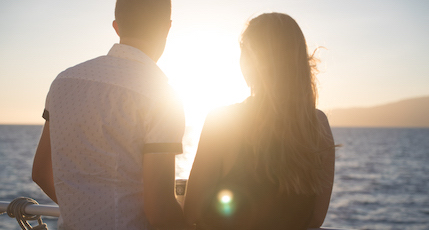 A couple looking at the sun from the deck of a cruise ship.